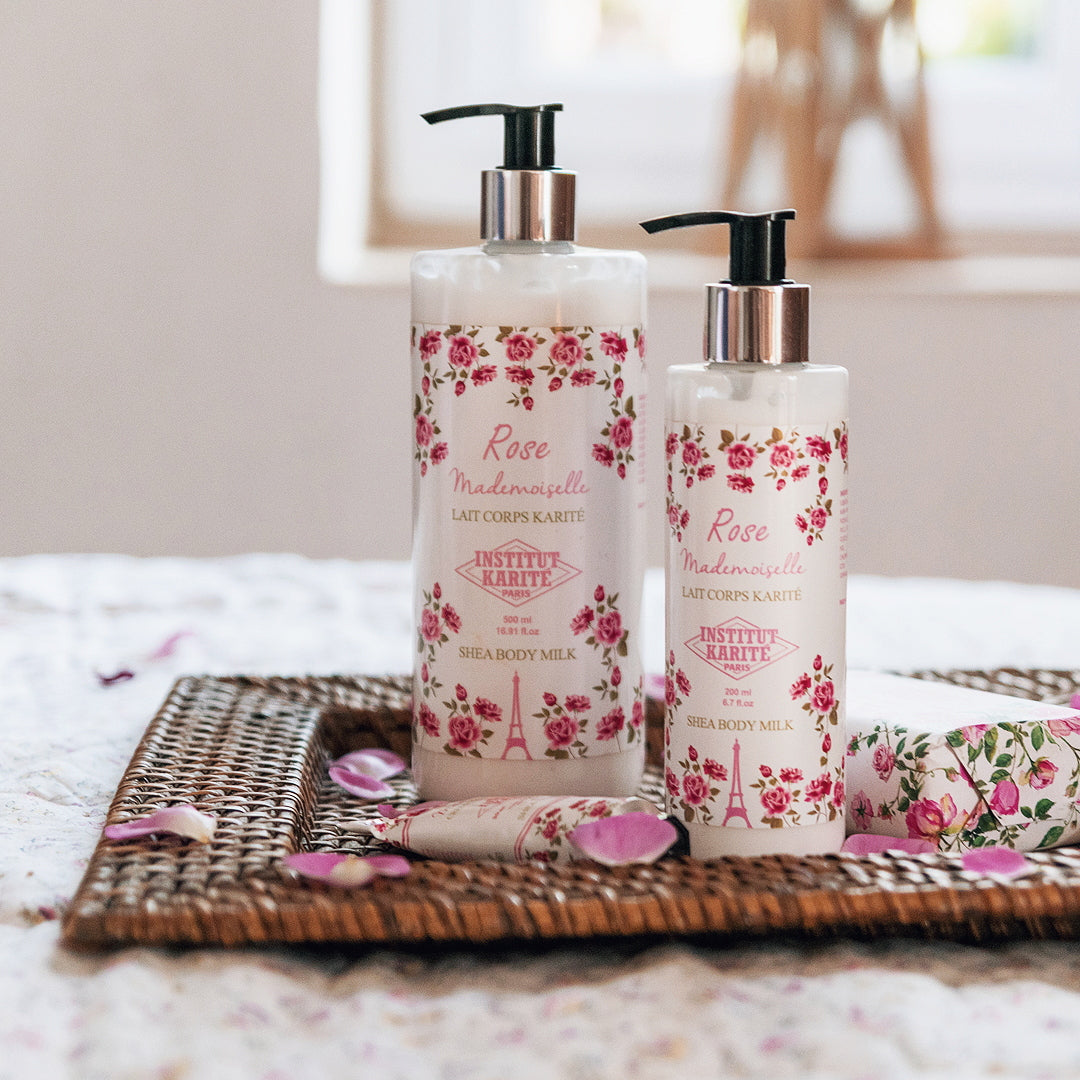 Rose Mademoiselle Shea Body Milk by Institut Karité Paris in two sizes on a woven tray with scattered rose petals