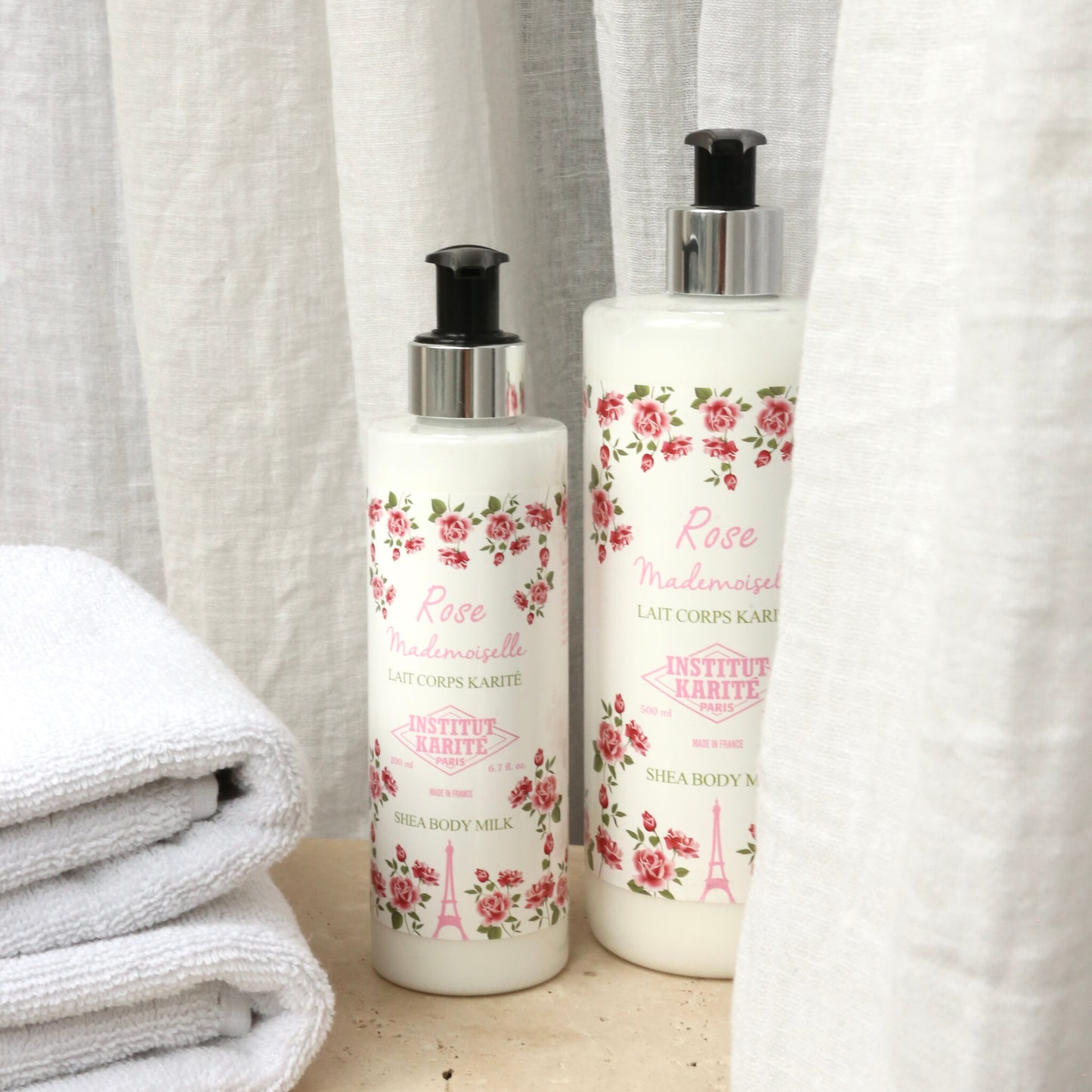 200mL and 500mL Rose Mademoiselle Shea Body Milk by Institut Karité Paris against linen with folded towels