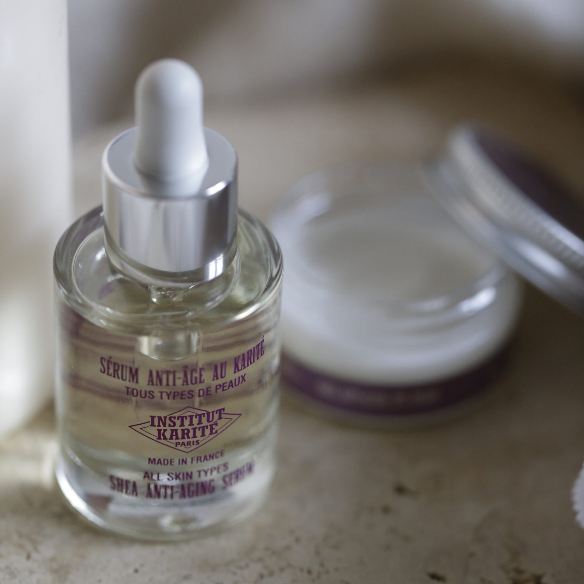 Shea Anti-Aging Serum bottle with its dropper beside an open cream jar