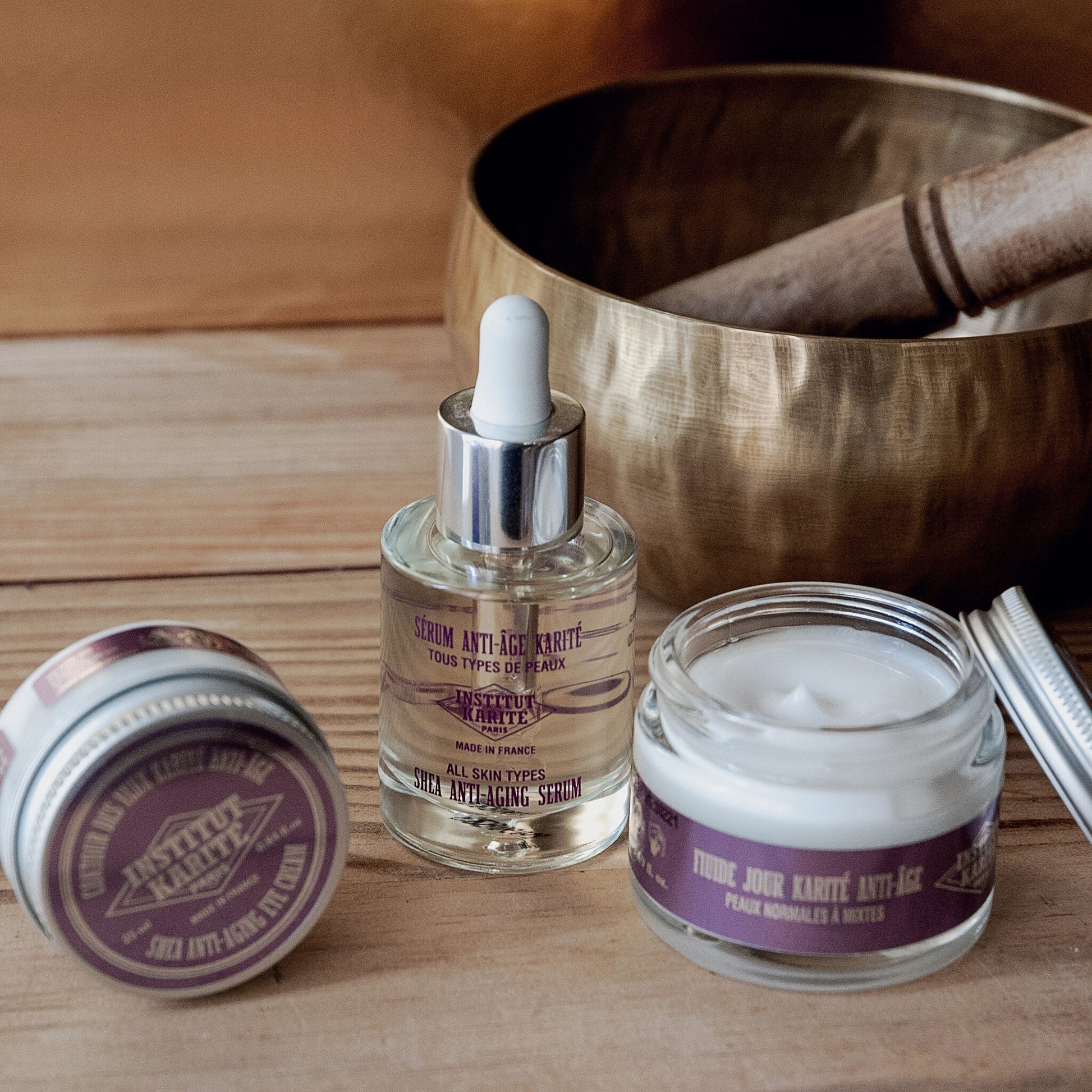 Shea Anti-Aging Serum with Shea Anti-Aging Eye Cream and day fluid on wood beside a brass bowl