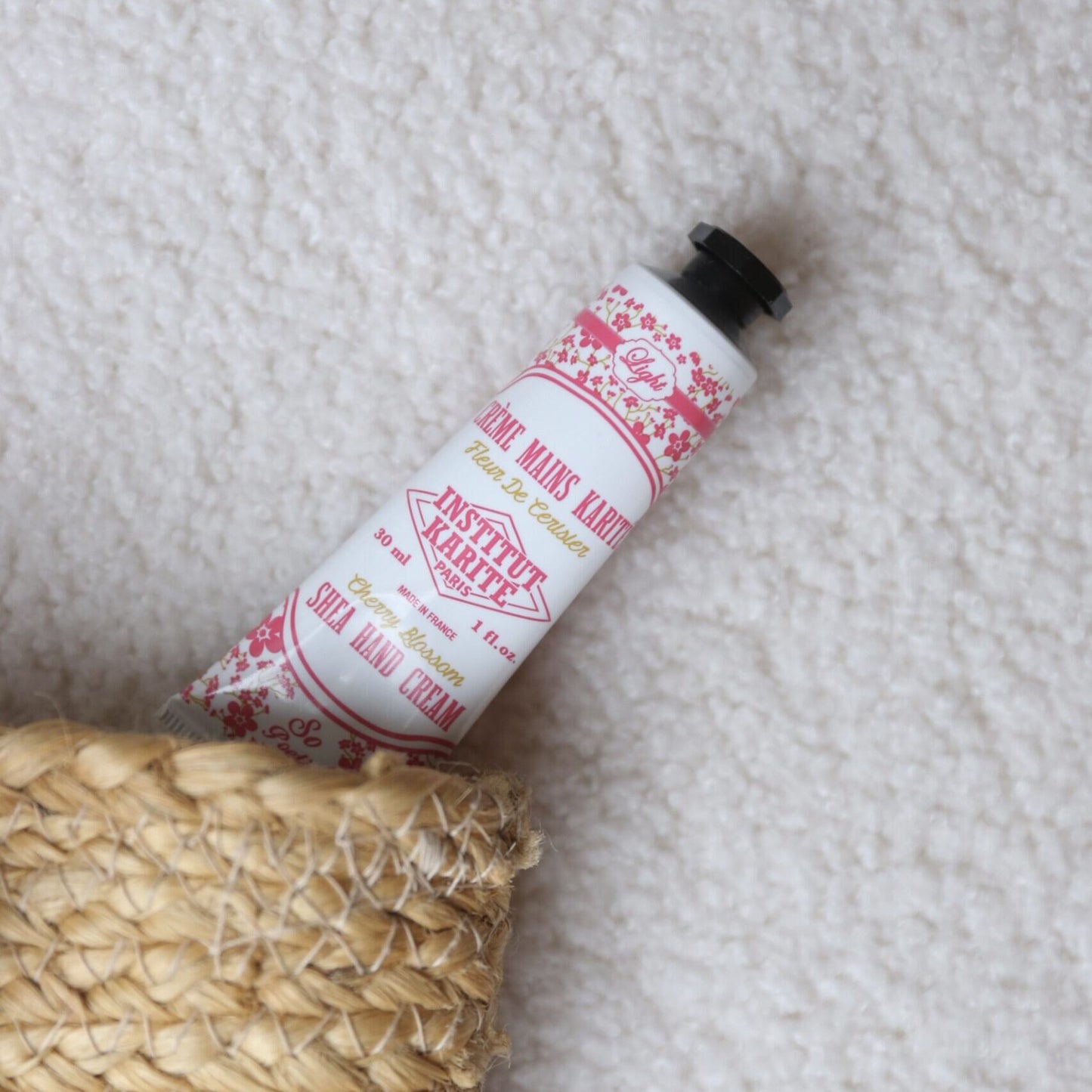 Cherry Blossom Shea Hand Cream 30ml tube resting on a woven basket and soft blanket