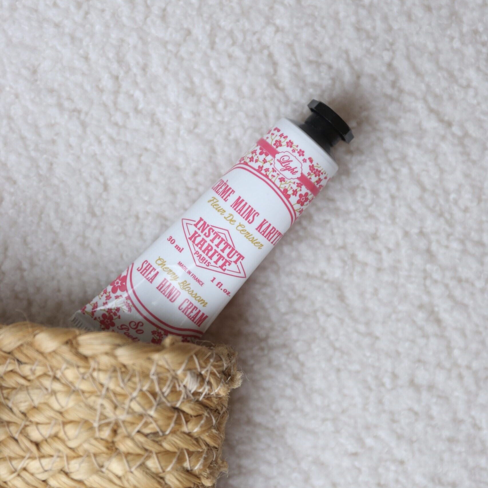 Cherry Blossom Shea Hand Cream 30ml tube resting on a woven basket and soft blanket