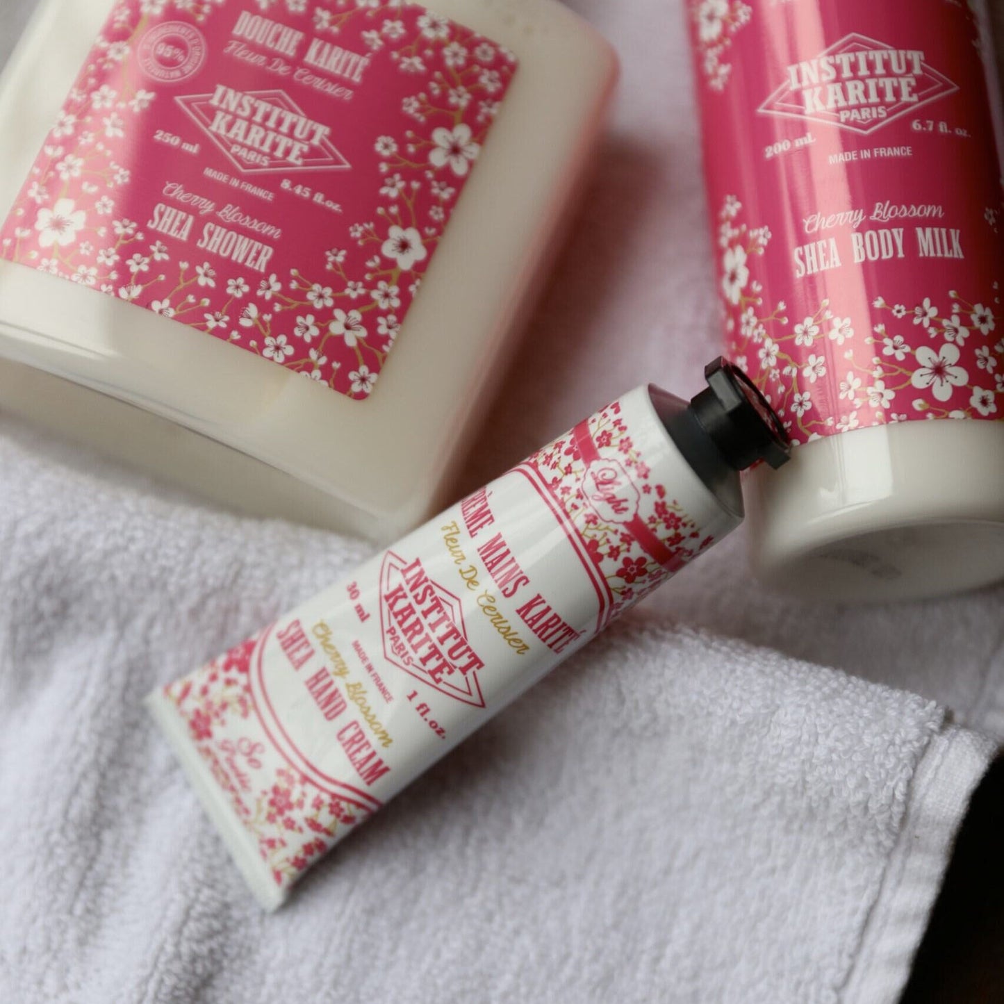Cherry Blossom Shea Hand Cream 30ml on a towel with Cherry Blossom Shea Shower and Body Milk