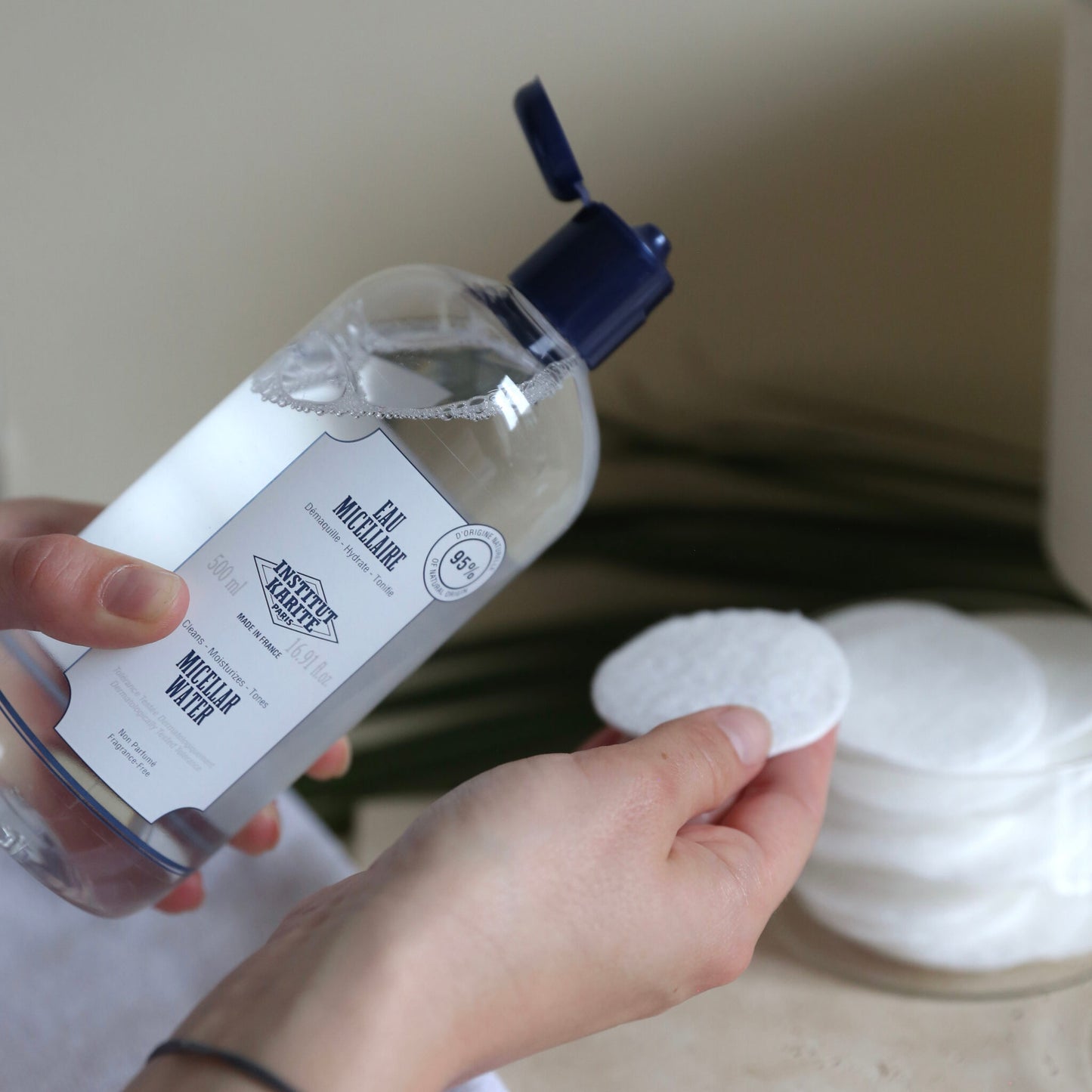 Hand holding the 500ml Micellar Water bottle beside a stack of cotton pads