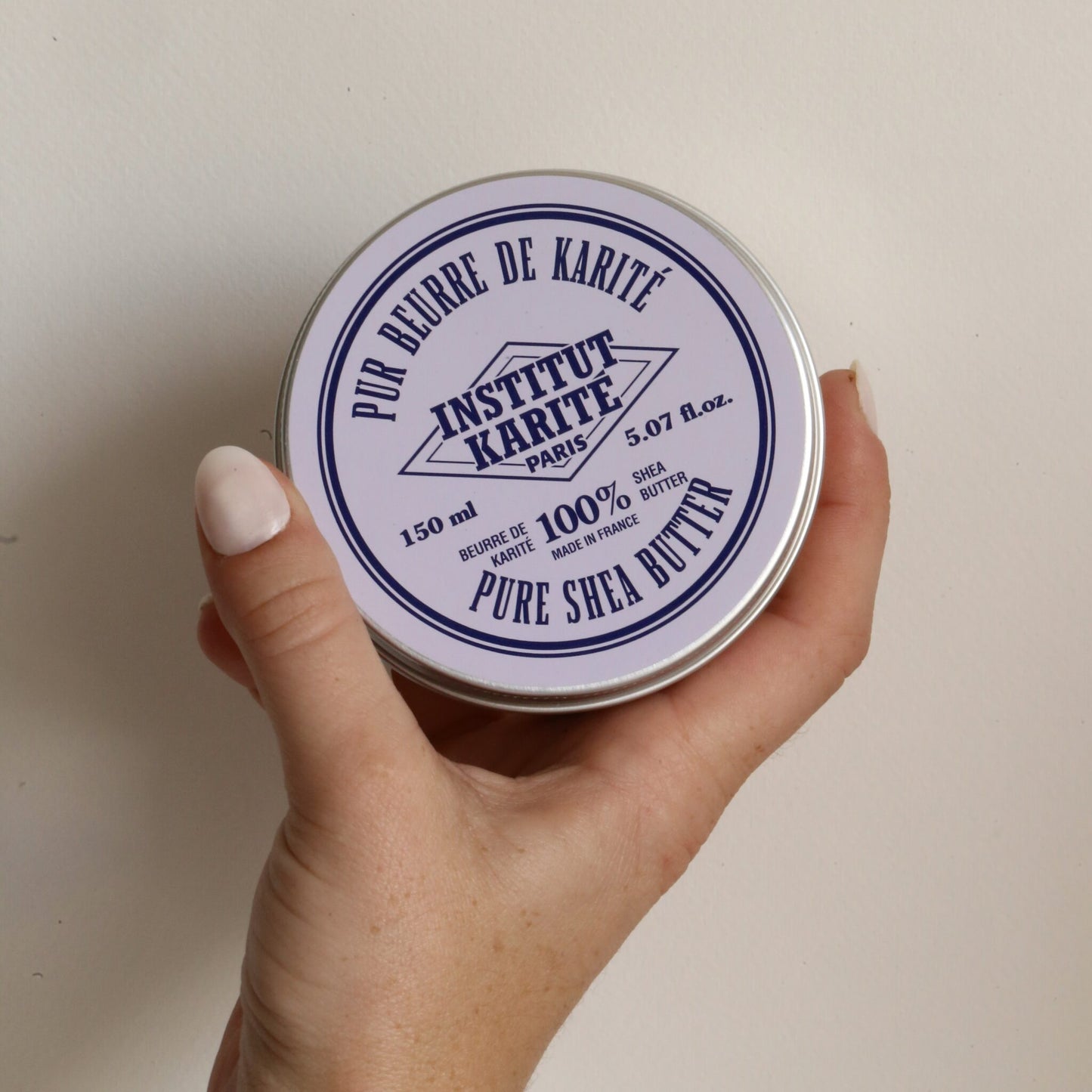 A hand holding the 150 ml tin of Institut Karité Paris Pure Shea Butter, showing its size