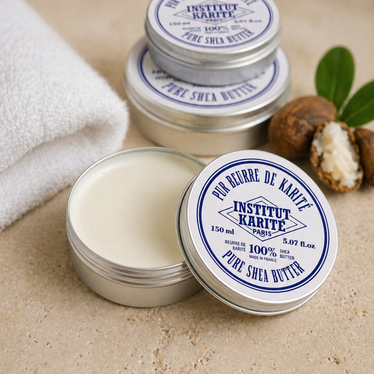 Open 150 ml tin of Institut Karité Paris Pure Shea Butter showing the cream inside, with shea nuts and a folded towel