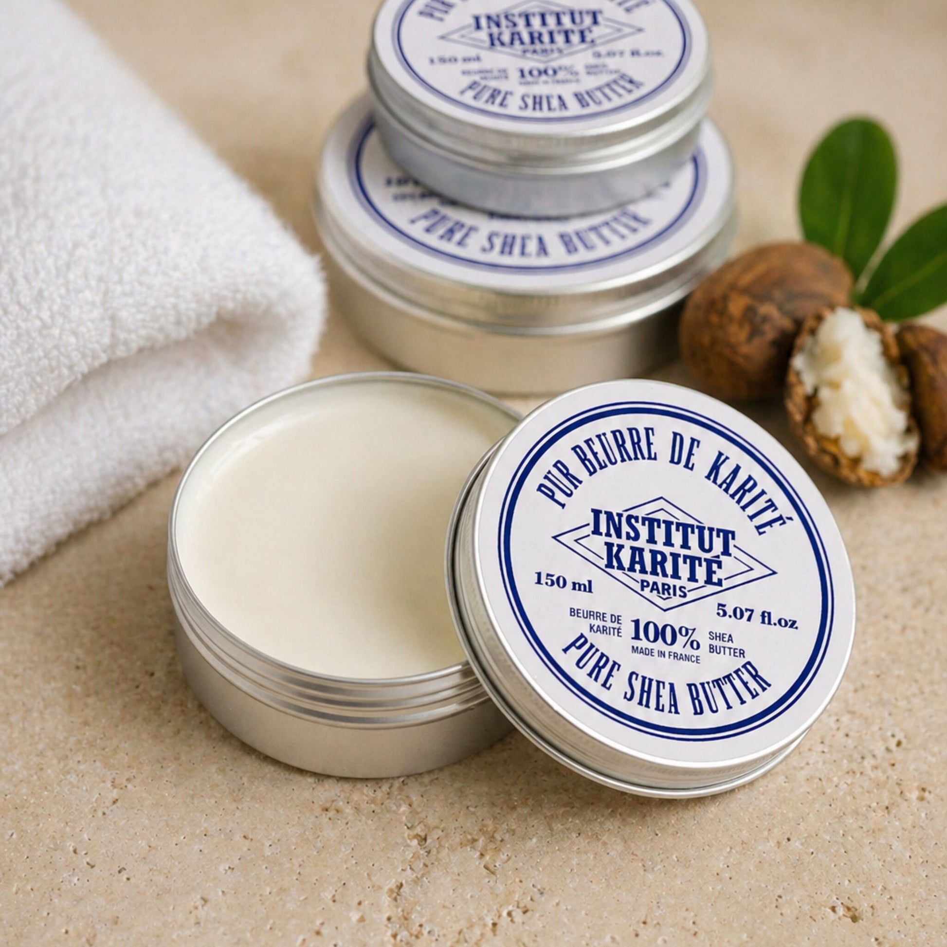 Open 150 ml tin of Institut Karité Paris Pure Shea Butter showing the cream inside, with shea nuts and a folded towel