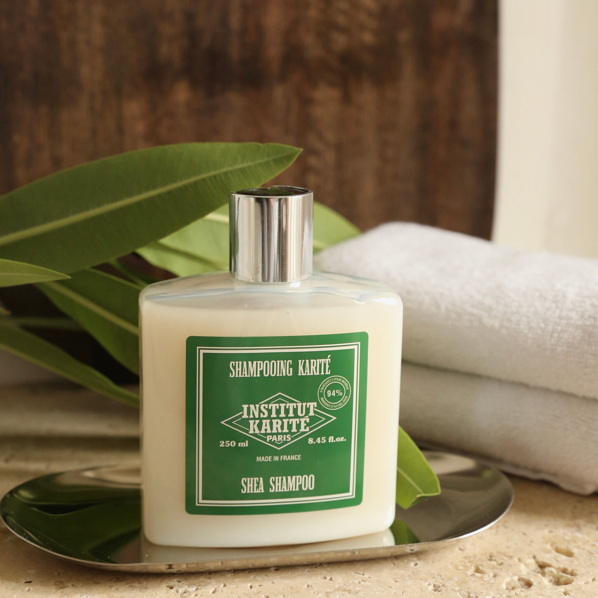 Shea Shampoo 250ml bottle on a silver tray with a folded towel and green foliage