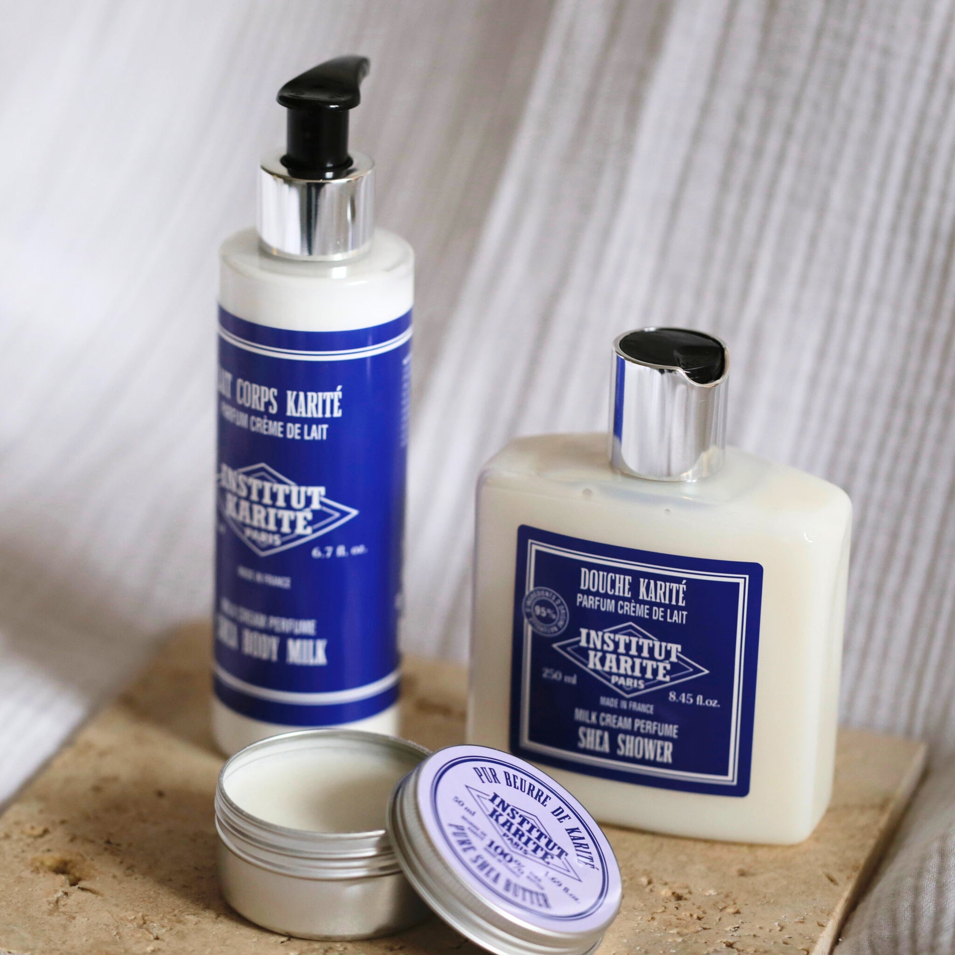 Shea Shower Milk Cream 250ml bottle with Shea Body Milk and an open tin of pure shea butter on stone