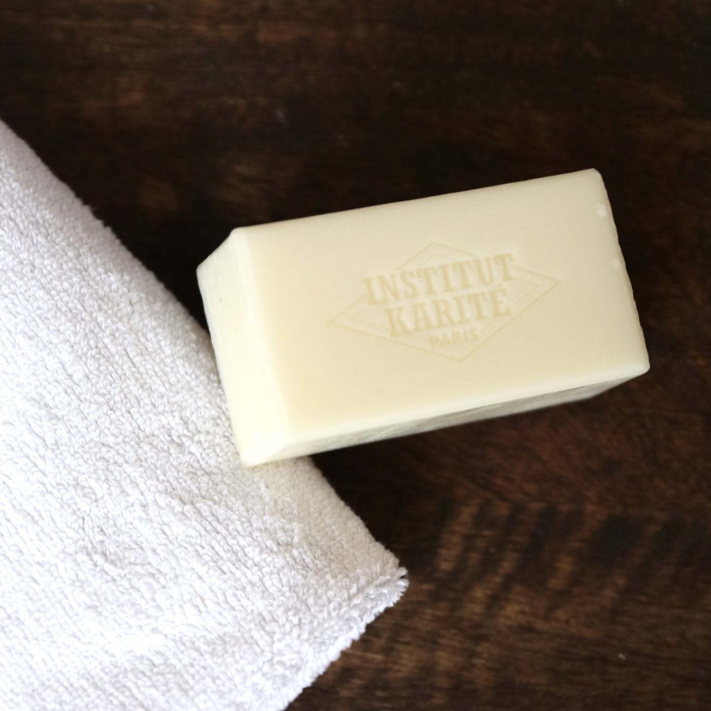Unwrapped 150g shea soap bar by Institut Karité Paris seen from above, resting on a white cotton towel on dark wood